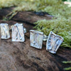 2 pairs of square ish odd melt studs sitting on a mossy log