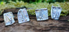 2 pairs of square ish odd melt studs sitting on a mossy log